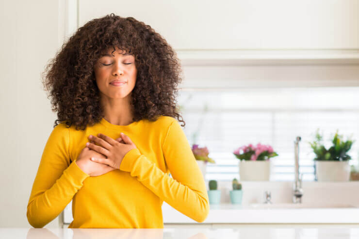 Gratitude Woman standing at kitchen counter, hands clasped at her chest with her eyes closed