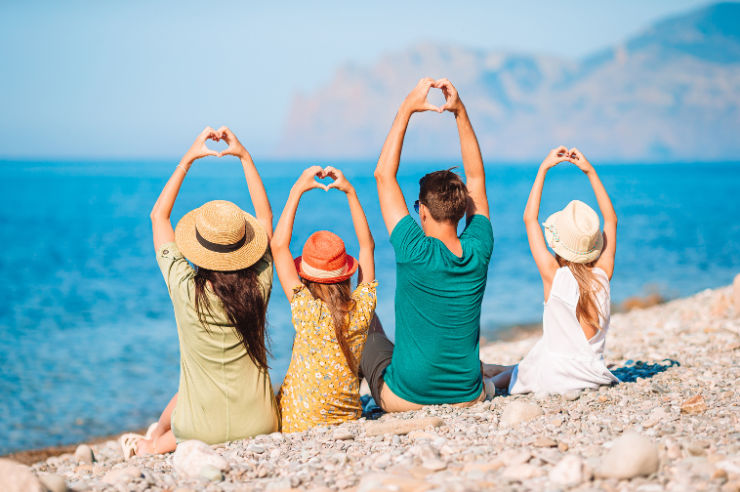 Photo of family with back to camera on a beach making hearts with their hands 